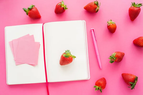 Vue du dessus du carnet et des notes collantes près des fraises fraîches sur fond rose — Photo de stock