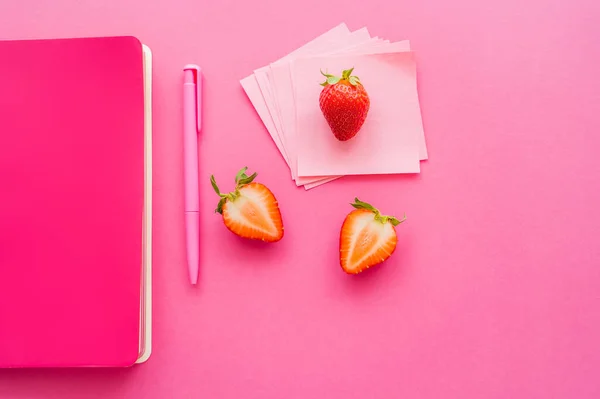 Vue de dessus des fraises bio près de notes collantes et carnet sur fond rose — Photo de stock