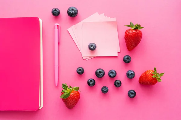 Вид зверху на ягоди біля липких нот і блокнот на рожевій поверхні — стокове фото