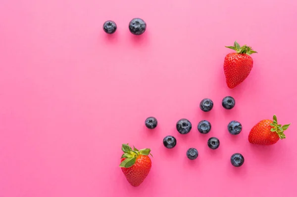 Vista superior de fresas naturales y arándanos en la superficie rosa - foto de stock