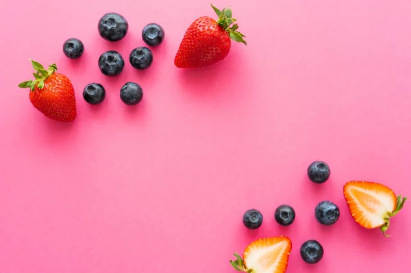 Vista superior de fresas y arándanos enteros en la superficie rosa - foto de stock