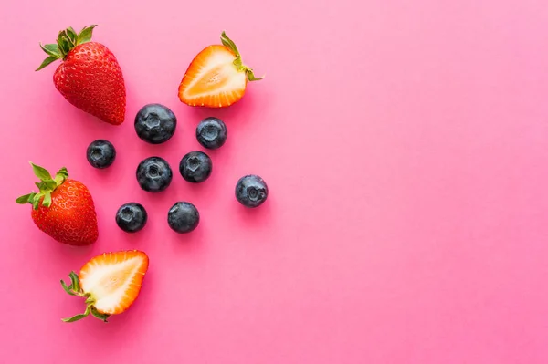 Vista superior de arándanos naturales y fresas sobre fondo rosa - foto de stock