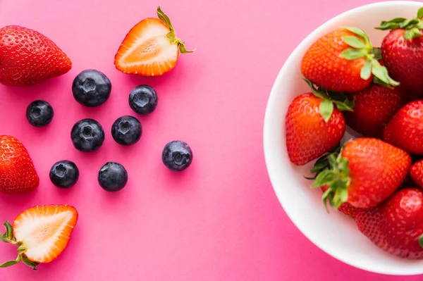 Vue de dessus des bleuets et fraises naturels dans un bol sur fond rose — Photo de stock