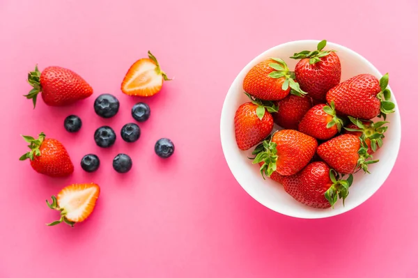 Vue du dessus des fraises douces dans un bol près des bleuets flous sur fond rose — Photo de stock