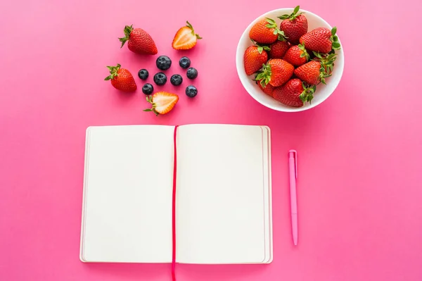 Top view of ripe berries near open notebook on pink background — Stock Photo