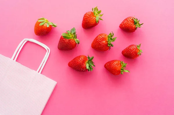 Vista dall'alto di fragole fresche con foglie vicino shopping bag su sfondo rosa — Foto stock