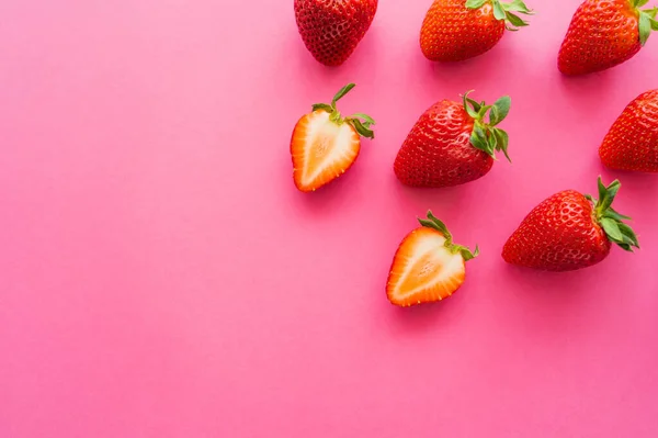 Draufsicht auf ganze und geschnittene Erdbeeren auf rosa Hintergrund — Stockfoto
