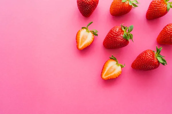 Vista superior de fresas enteras y cortadas sobre fondo rosa - foto de stock