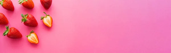 Draufsicht auf geschnittene und ganze Erdbeeren auf rosa Hintergrund mit Kopierraum, Banner — Stockfoto