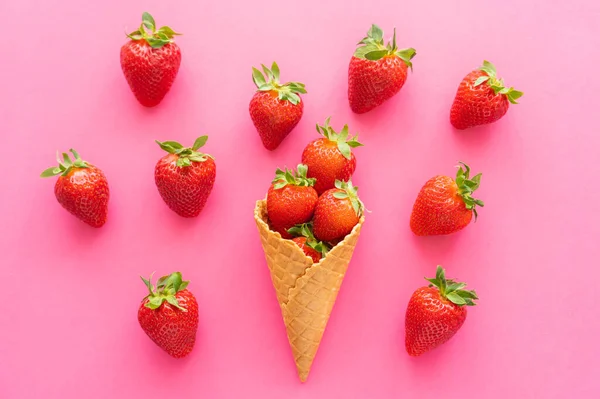 Draufsicht auf reife Erdbeeren und Waffelkegel auf rosa Hintergrund — Stockfoto