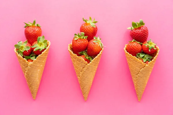 Colocação plana com morangos em cones de waffle no fundo rosa — Fotografia de Stock