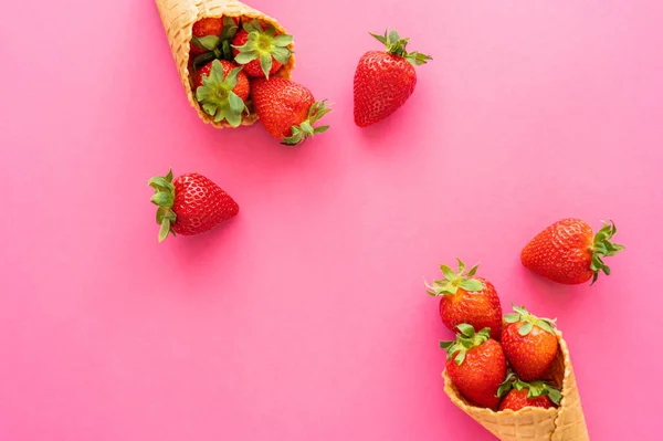 Draufsicht auf frische Erdbeeren mit Blättern in Waffelkegeln auf rosa Hintergrund — Stockfoto