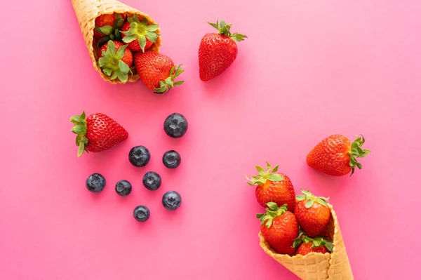 Top view of strawberries and blueberries near waffle cones on pink background — Stock Photo