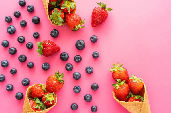 Flat lay with fresh berries and waffle cones on pink background — Stock Photo