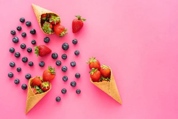 Flat lay with blueberries and strawberries and waffle cones on pink surface — Stock Photo