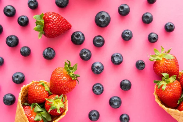 Flat lay with blueberries near strawberries in waffle cones on pink background — Stock Photo