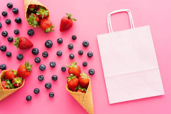 Flache Liege mit Einkaufstasche neben frischen Beeren und Waffeltüten auf rosa Hintergrund — Stockfoto