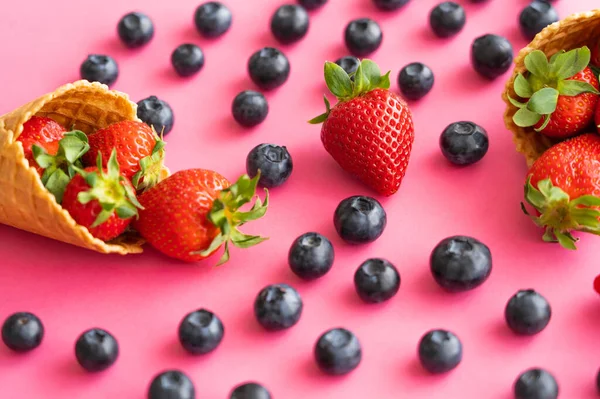 Vue rapprochée des bleuets flous près des cônes de gaufres avec des fraises sur fond rose — Photo de stock