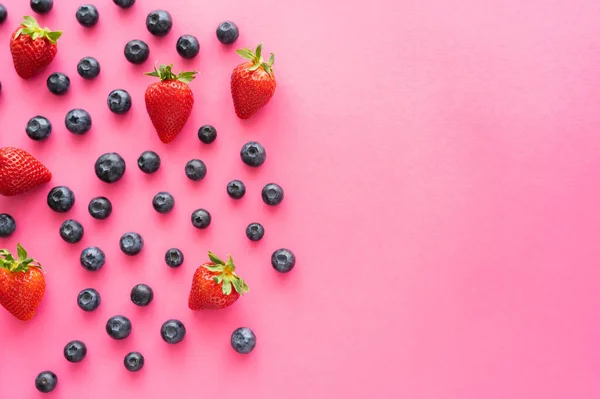 Acostado plano con arándanos y fresas en la superficie rosa - foto de stock