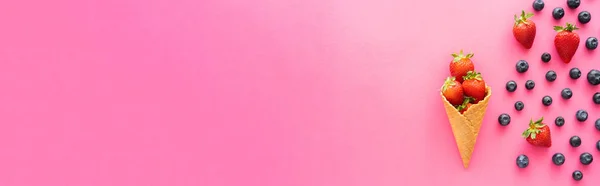 Flat lay with blueberries near juicy strawberries in waffle cone on pink background, banner — Stock Photo