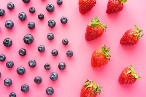 Tendido plano de arándanos jugosos cerca de fresas sobre fondo rosa - foto de stock