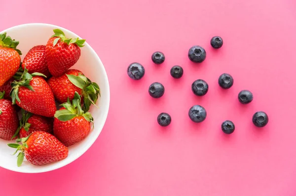 Top view of strawberries in bowl near blueberries on pink background — Stock Photo