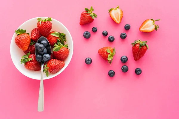 Top view of organic blueberries and strawberries in bowl on pink surface — Stock Photo