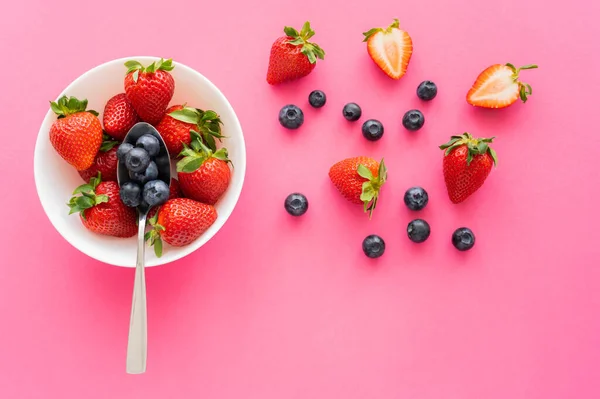 Vista superior de arándanos orgánicos y fresas en un tazón sobre una superficie rosada - foto de stock