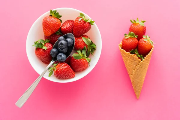 Vista superior de bagas em tigela e cone de waffle no fundo rosa — Fotografia de Stock