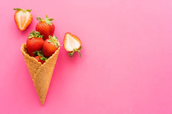 Draufsicht auf süße Waffelkegel und Erdbeeren auf rosa Hintergrund — Stockfoto