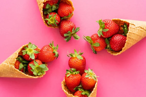 Flat lay com deliciosos cones de waffle com morangos em fundo rosa — Fotografia de Stock