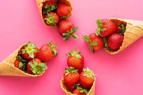 Posa piatta con deliziosi coni di cialde con fragole su sfondo rosa — Foto stock