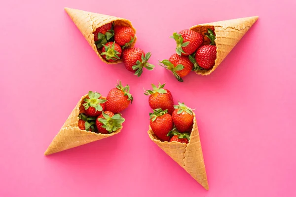 Poser à plat avec des fraises biologiques dans des cônes de gaufres sucrées sur fond rose — Photo de stock