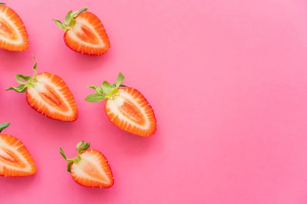 Colocación plana de fresas frescas cortadas sobre fondo rosa - foto de stock