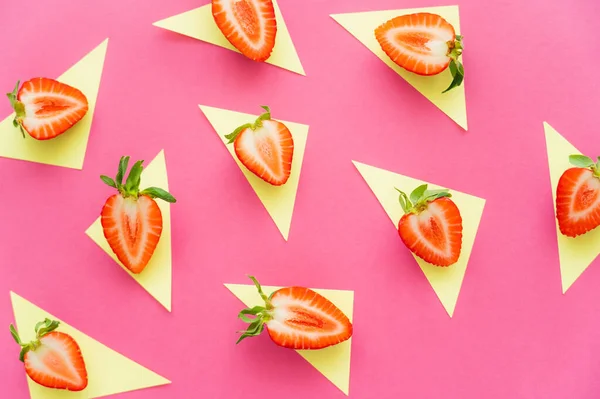 Flache Lage mit geschnittenen Erdbeeren auf gelben Dreiecken auf rosa Hintergrund — Stockfoto