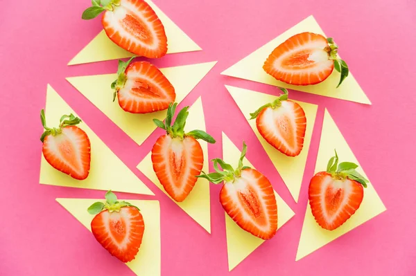 Colocación plana de fresas sobre triángulos amarillos sobre fondo rosa - foto de stock