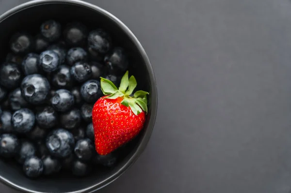 Top view of ripe strawberry in bowl with blueberries on black background — Stock Photo