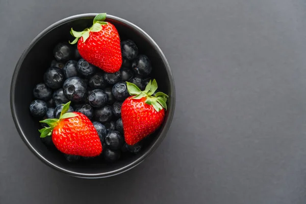 Top view of juicy strawberries on blueberries in bowl on black background — Stock Photo