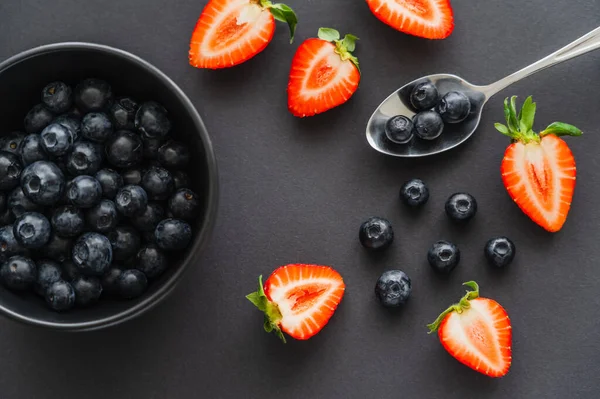 Top view of fresh berries near spoon and bowl on black background — Stock Photo