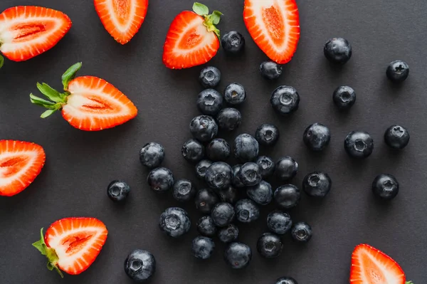 Top view of whole blueberries and cut strawberries on black background — Stock Photo