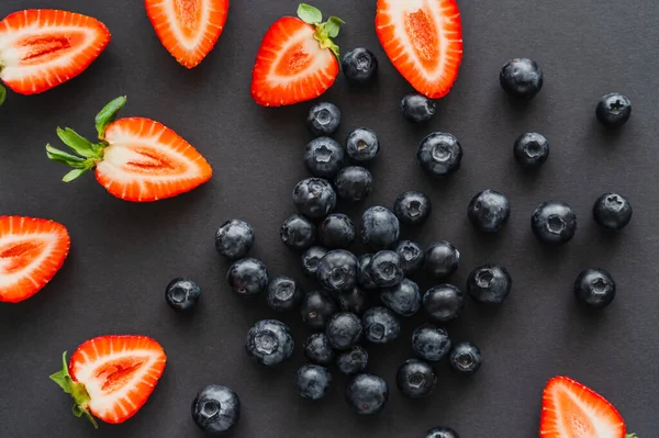 Vista superior de arándanos enteros y fresas cortadas sobre fondo negro - foto de stock