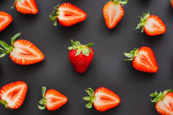 Flat lay com morango inteiro perto de cortar bagas no fundo preto — Fotografia de Stock