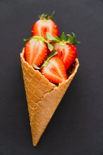 Vista superior del cono de gofre con fresas cortadas sobre fondo negro - foto de stock