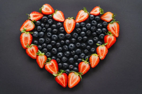 Flat lay with heart shape from berries on black background — Stock Photo