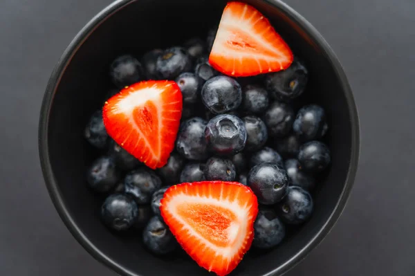 Top view of red strawberries and blueberries in bowl on black background — Stock Photo