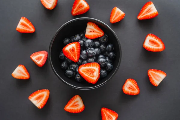 Top view of blueberries in bowl near strawberries on black background — Stock Photo