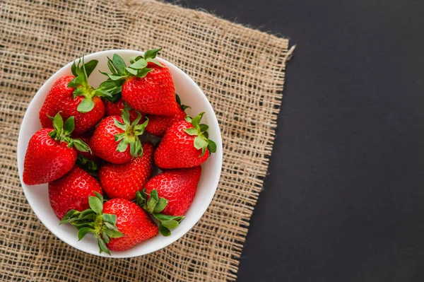 Draufsicht auf Bio-Erdbeeren in Schale auf Sacktuch auf schwarzem Hintergrund — Stockfoto