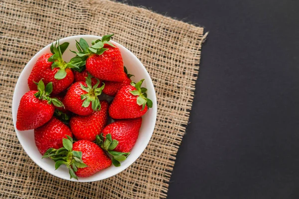 Top view of organic strawberries in bowl on sackcloth on black background — Stock Photo