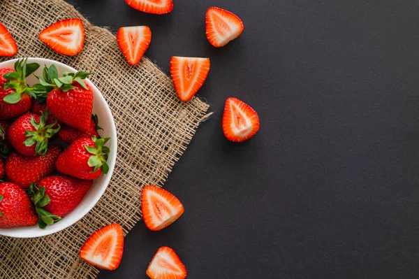 Draufsicht auf saftige Erdbeeren in Schale auf Sacktuch auf schwarzem Hintergrund — Stockfoto