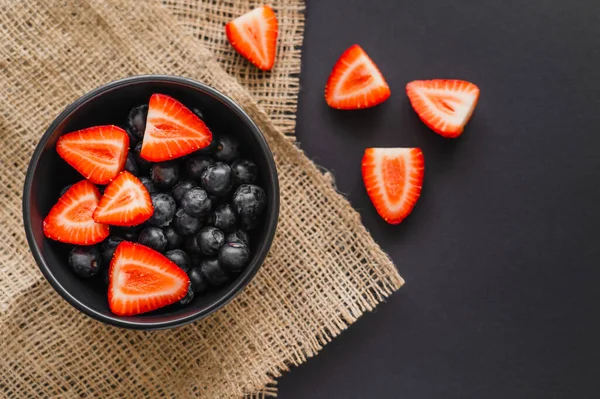 Top view of natural berries in bowl on sackcloth on black background — Stock Photo